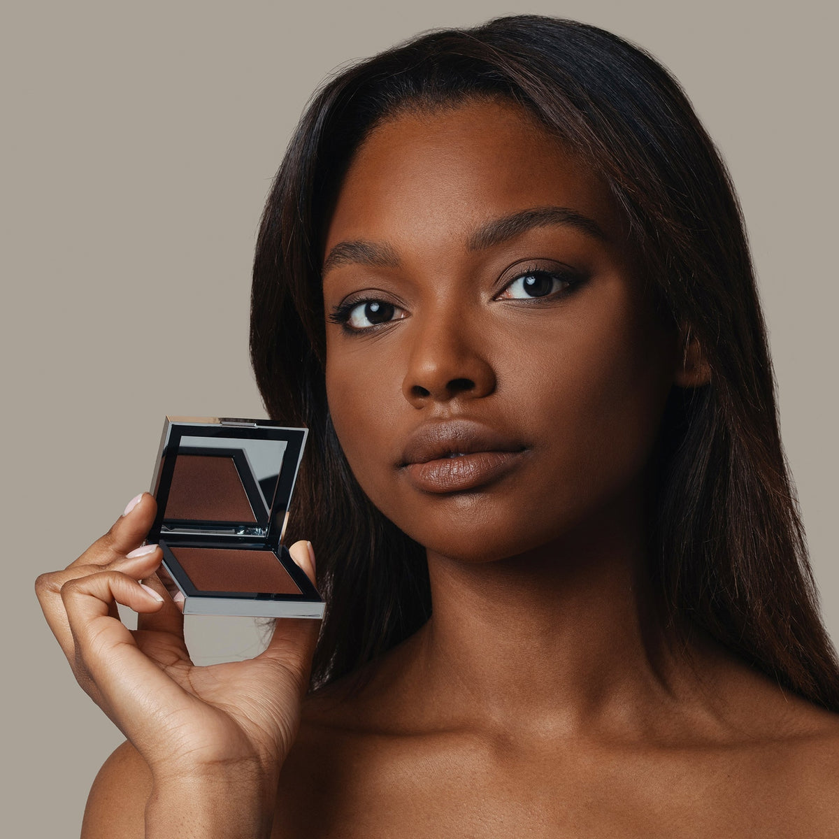 Eine Frau hält den geöffneten Skin Mate Compact von Mesauda Beauty in der Nähe ihres Gesichts und blickt in Kamera.