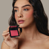 Eine Frau hält den geöffneten Skin Mate Compact von Mesauda Beauty in der Nähe ihres Gesichts und blickt in die Ferne.