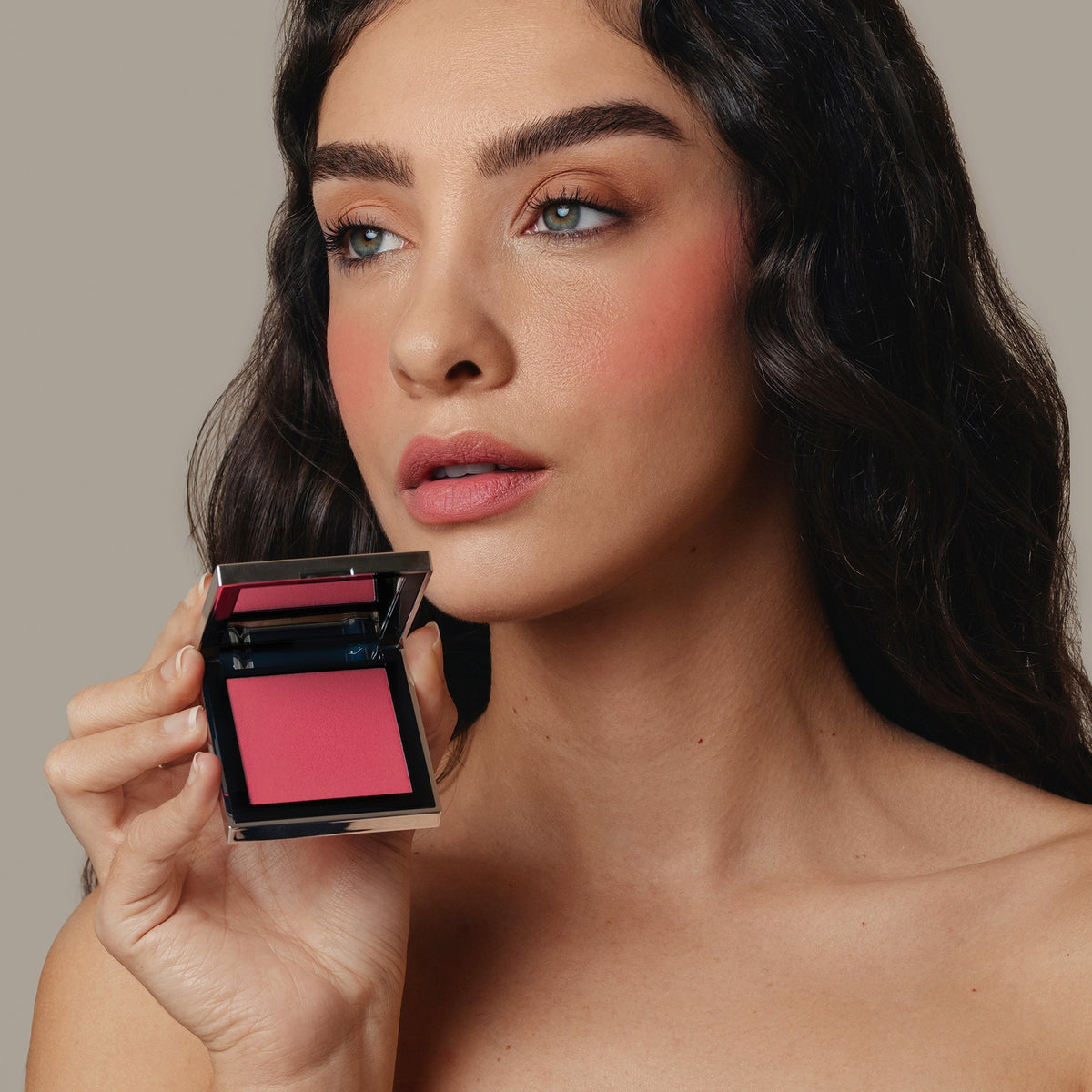 Eine Frau hält den geöffneten Skin Mate Compact von Mesauda Beauty in der Nähe ihres Gesichts und blickt in die Ferne.