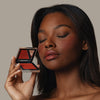 Eine Frau hält den geöffneten Skin Mate Compact von Mesauda Beauty in der Nähe ihres Gesichts und hat die Augen geschlossen.
