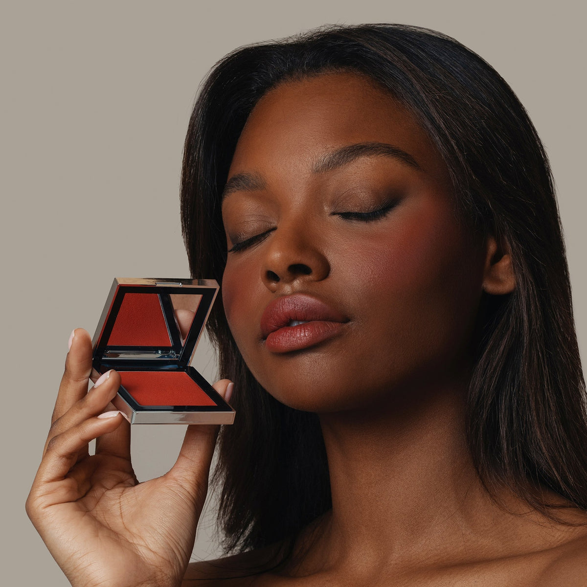 Eine Frau hält den geöffneten Skin Mate Compact von Mesauda Beauty in der Nähe ihres Gesichts und hat die Augen geschlossen.
