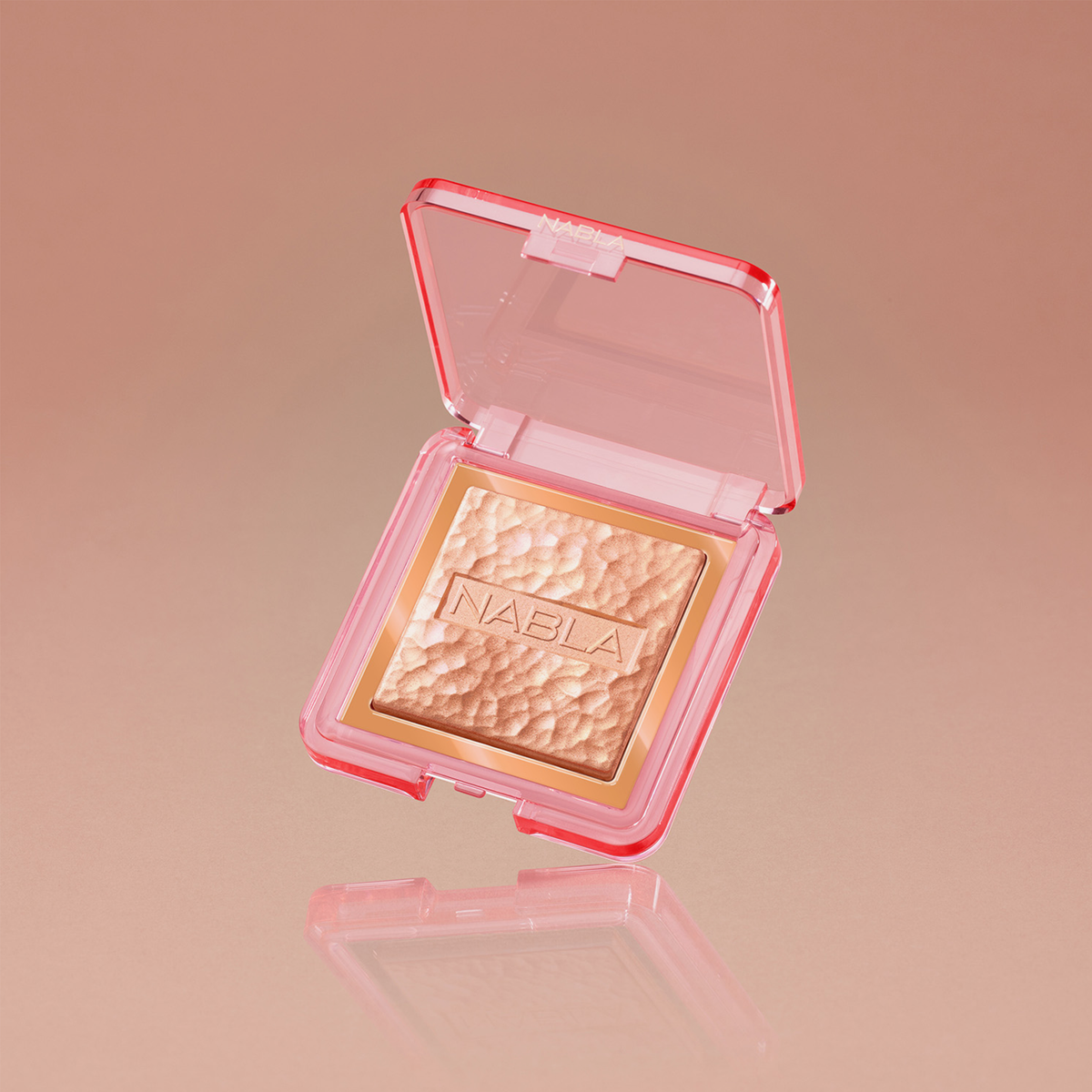 Ein goldener Highlighter in einem rosafarbenen transparenten Kompaktetui mit der Aufschrift NABLA, präsentiert auf einem pfirsichfarbenen Hintergrund.