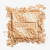 Ein quadratischer, goldener Skin Glazing-Presspuder mit der Prägung „NABLA“ auf der Oberseite, umgeben von zerstoßenen Stücken.