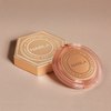 Runder, transparenter Puder mit NABLA-Logo und sechseckige, goldene Box mit der Aufschrift „Close-Up Smoothing Pressed Powder“ auf beigem Grund.