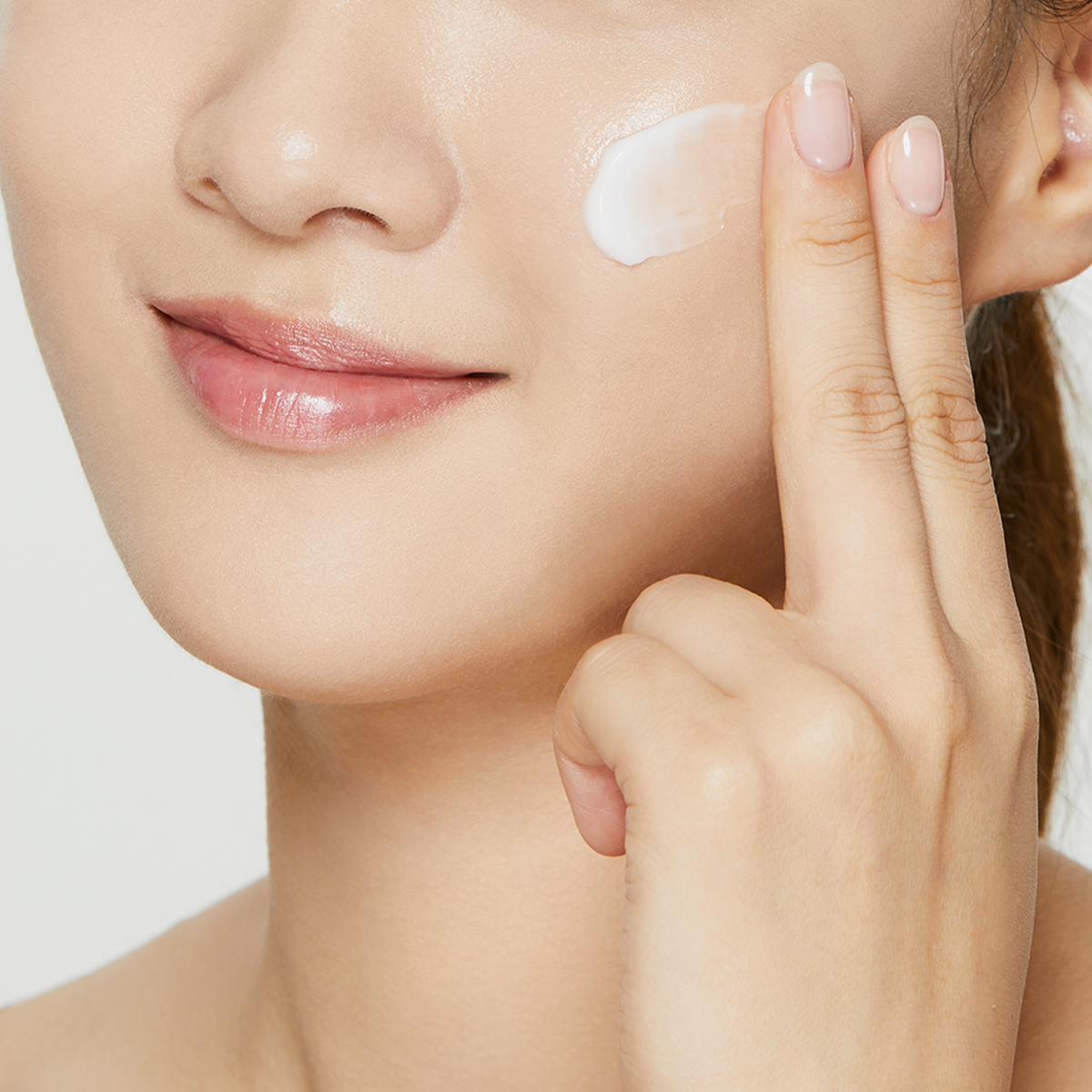 Eine Frau lächelt leicht, während sie mit ihren Fingern die Ultimate Nourishing Rice Overnight Spa Mask auf ihre Wange aufträgt.