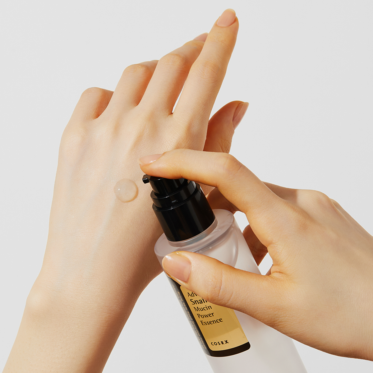 Vor einem weißen Hintergrund gibt eine Hand die klare Advanced Snail 96 Mucin Power Essence aus der Pumpflasche auf den Handrücken.