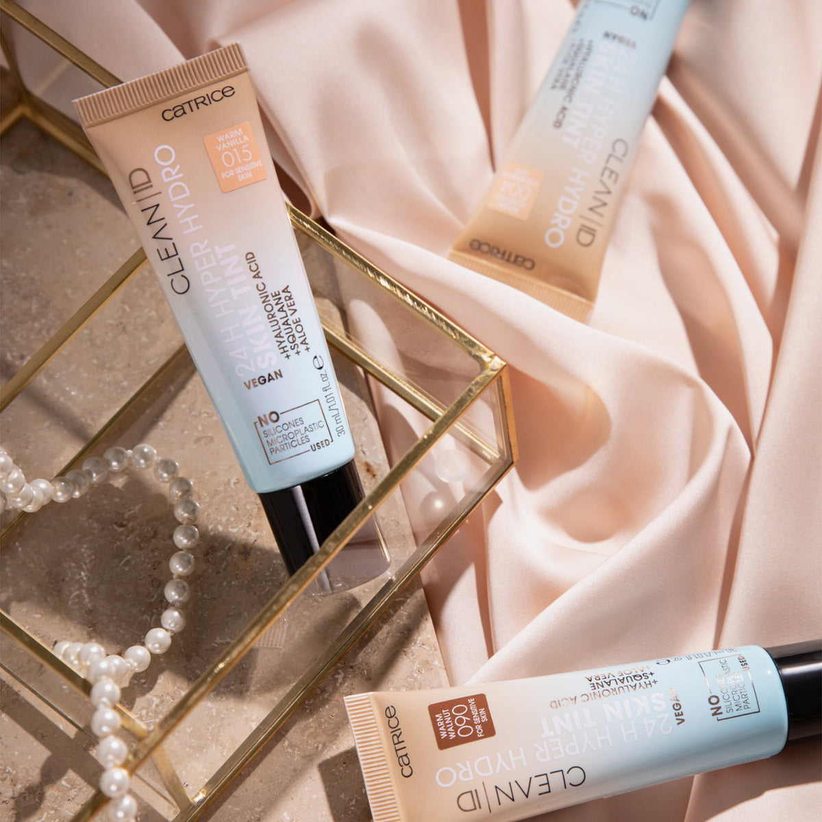 Mehrere Tuben Catrice Clean ID 24H Hyper Hydro Skin Tint auf einem beigen Seidentuch und in einer Schmuckschatulle.