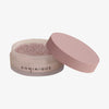 Offenes Glas mit Smooth & Blur Setting Powder, einem losen Puder-Make-up mit einem rosa Deckel mit der Aufschrift DOMINIQUE auf weißem Hintergrund.