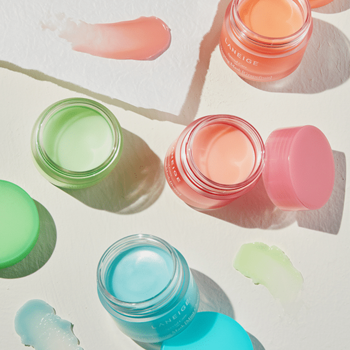Vier bunte, geöffnete Tiegel der Laneige Lip Sleeping Mask EX mit Produktmustern auf hellem Hintergrund.