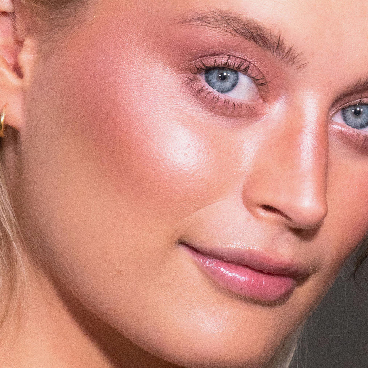 Nahaufnahme einer Person mit strahlender Haut, blauen Augen und glänzenden Lippen, die LH Cosmetics Duo Dimension Area für einen Hauch von rosa Rouge trägt.