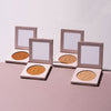 Vier geöffnete LH Cosmetics Infinity Bronzer präsentiert auf einem rosa-weißen Hintergrund.