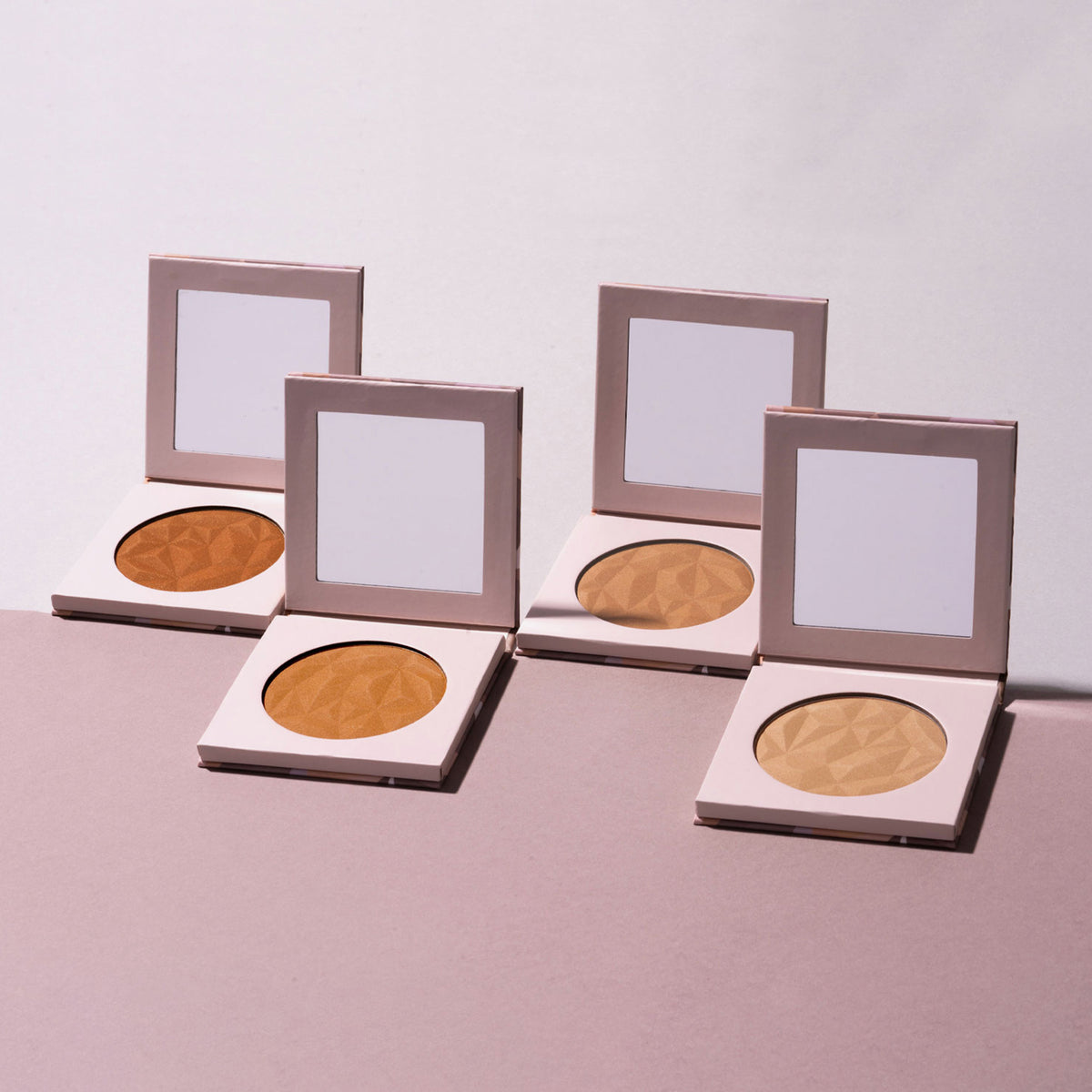 Vier geöffnete LH Cosmetics Infinity Bronzer präsentiert auf einem rosa-weißen Hintergrund.