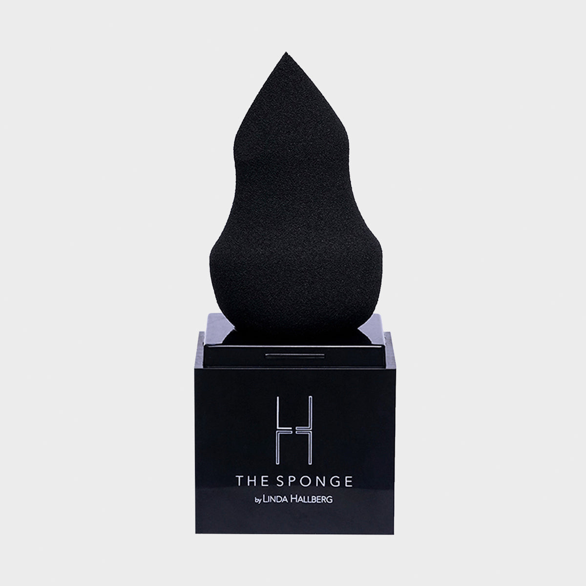 Auf einem schwarzen Ständer ist ein schwarzer Make-up-Schwamm „The Sponge“ von LH Cosmetics vor einem weißen Hintergrund abgebildet.