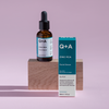 Die Flasche und die Schachtel des Zink-PCA-Gesichtsserums werden auf einem Holzblock mit rosa Hintergrund präsentiert.
