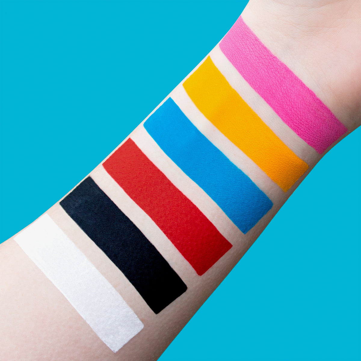 Das Bild zeigt einen Arm mit sieben deckenden Farbswatches der SUVA Beauty OPAKES Cosmetic Paints;  aufgetragen auf heller Haut vor türkisfarbenem Hintergrund.