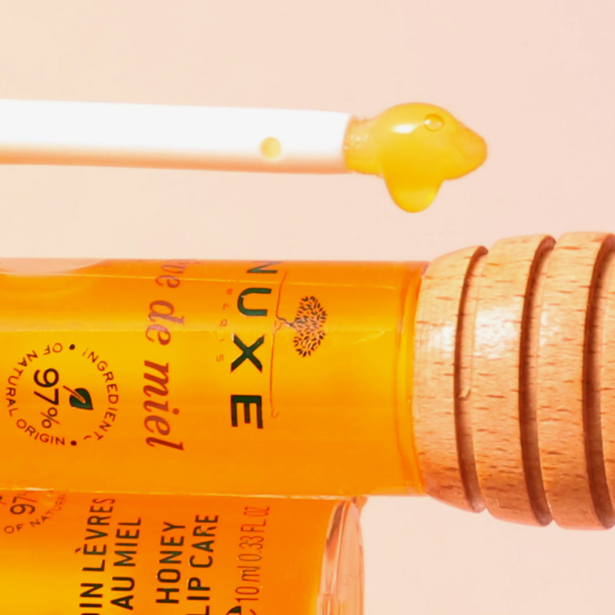Applikatorstab mit gelbem Lippenbalsam neben einer Tube NUXE Honey Lip Care Rêve de Miel und einem hölzernen Honiglöffel.