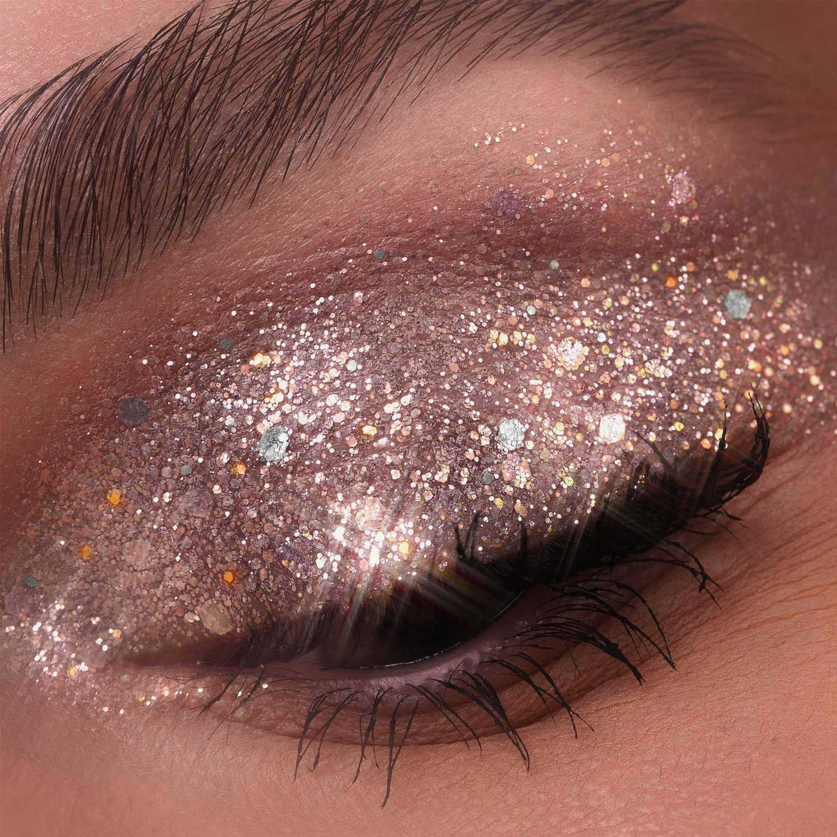 Ein geschlossenes Auge besticht durch den faszinierenden, mehrfarbigen Schimmer der Glorious Lights Glitter Palette und lange, dunkle Wimpern.
