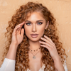 Eine Frau mit langem, lockigem, rotem Haar und leichtem Make-up posiert mit ihren Händen vor ihrem Gesicht vor einem beigen Hintergrund und präsentiert die Transition Palette.