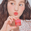 Eine Frau in einem weißen Top mit Punkten spitzt die Lippen, während sie Laneiges Lip Sleeping Mask EX hält.