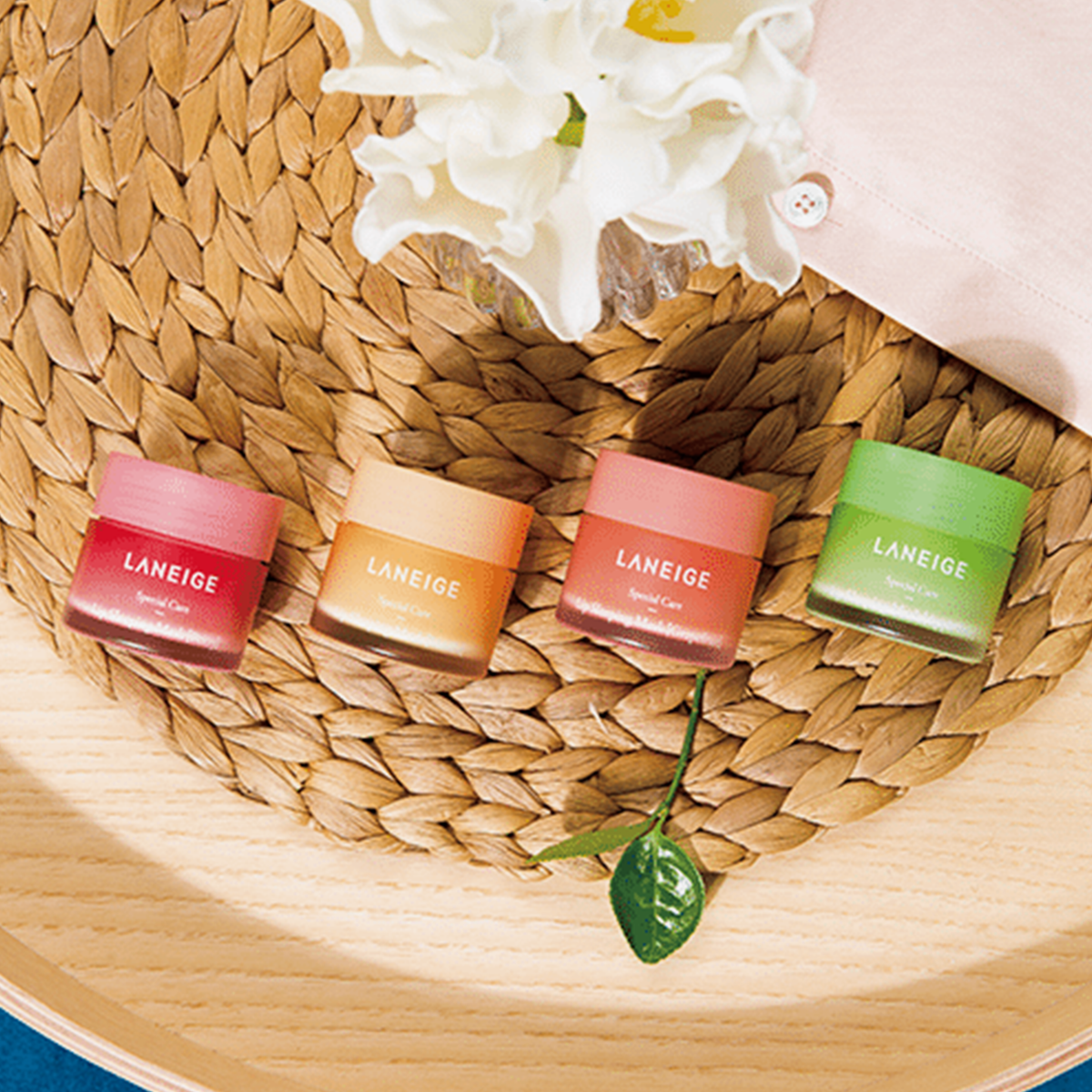 Vier farbenfrohe Tiegel der Laneige Lip Sleeping Mask EX auf einer gewebten Bastmatte platziert.