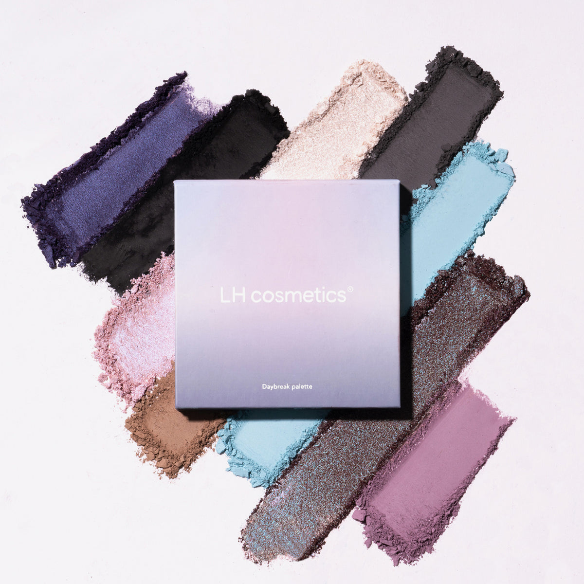 Violette Daybreak Palette von LH Cosmetics wird auf weißem Hintergrund angezeigt, umgeben von zerkleinerten Lidschatten in mehreren Farben.