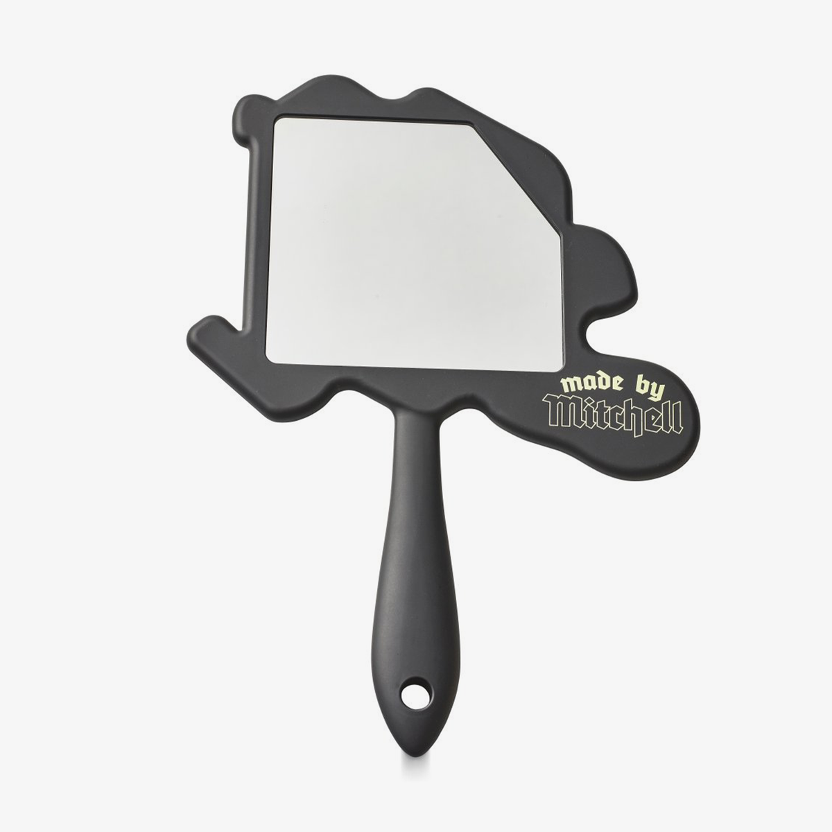Der Made By Mitchell Mirror ist ein schwarzer Handspiegel in M-Form und dem Schriftzug Made by Mitchell" in Gold an der Seite.