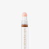Nahaufnahme der weiß-goldenen Tube Re-Generation Concealer in der Farbe Warm Honey mit rosafarbener Schwammspitze – für gebräunte Haut mit warmem Unterton.