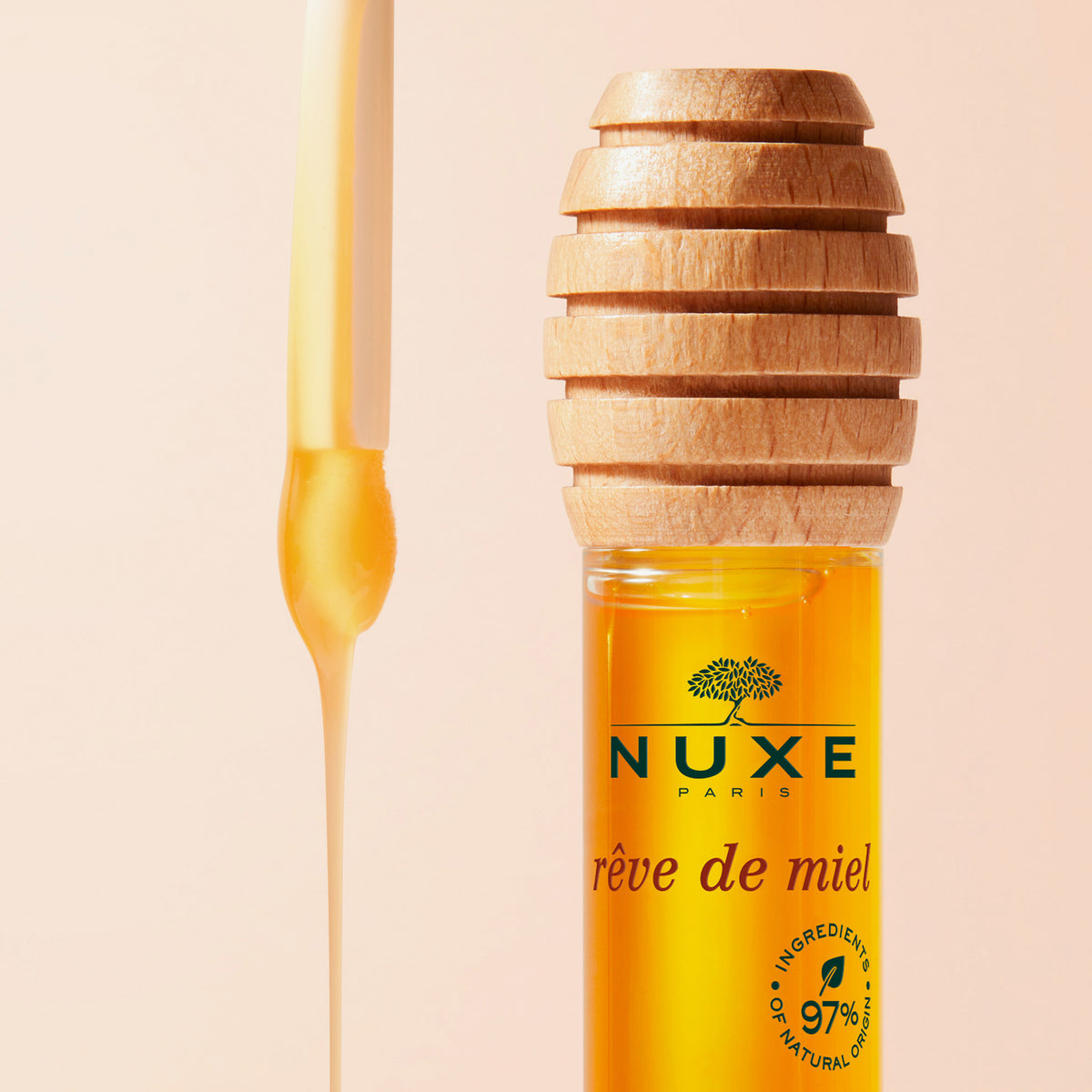 NUXE Rêve de Miel Lippenöl in honigfarbener Flüssigkeit mit Holzapplikator, daneben tropfender Honig, auf hellem Hintergrund.