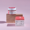 Ein Tiegel und eine Schachtel Collagen Face Cream präsentiert auf einem Holzblock vor einem rosa Hintergrund.