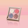 Schräg platzierte NABLA „Miami Lights“ Glitter Palette mit vier Glitzertönen, vor einem glänzenden Hintergrund in Pfirsich-Rosa-Verlauf.