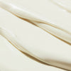Nahaufnahme der NUXE Sun Delicious Lotion High Protection zeigt ihre glatte, cremeweiße Textur mit weichen, fließenden Rillen.