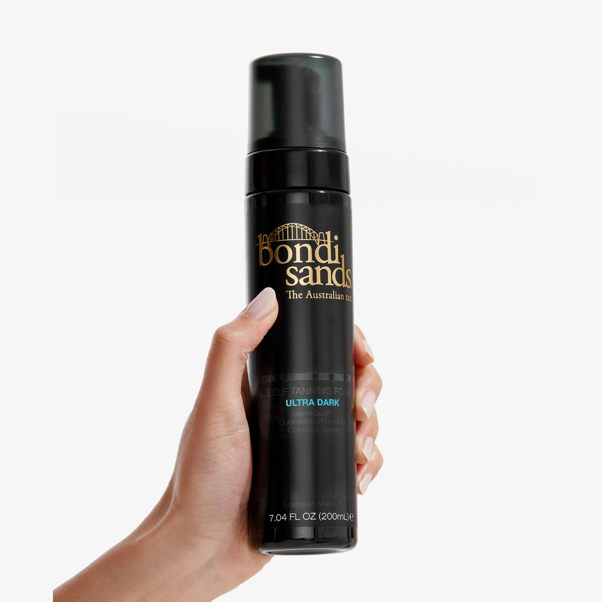 Hand hält eine schwarze Flasche Bondi Sands Self Tanning Foam Ultra Dark vor einem weißen Hintergrund