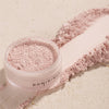 Öffnen Sie den Tiegel mit Smooth & Blur Setting Powder, einem rosafarbenen losen Puder, und verteilen Sie das Produkt auf einer hellen Oberfläche.