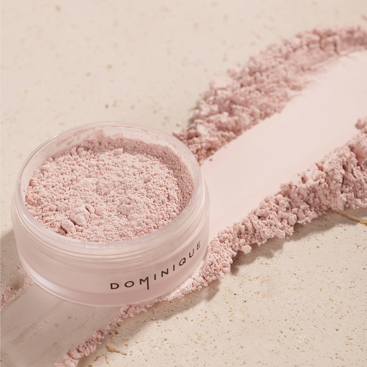 Öffnen Sie den Tiegel mit Smooth & Blur Setting Powder, einem rosafarbenen losen Puder, und verteilen Sie das Produkt auf einer hellen Oberfläche.