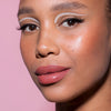 Frau mit strahlender Haut trägt kräftige Lippen mit LH Cosmetics Crayon Lipliner und weißem grafischem Eyeliner vor einem rosa Hintergrund.