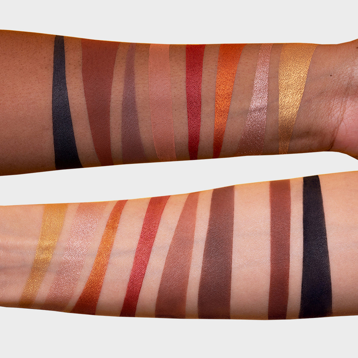 Auf zwei Unterarmen mit unterschiedlichen Hauttönen sind neutrale und erdige Farbmuster der Infinity Deep Palette von LH Cosmetics zu sehen.