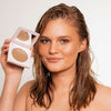 Eine Frau mit strahlendem warmen Make-up lächelt in die Kamera und einen Infinity Bronzer in der Farbe Beyond von LH Cosmetics.