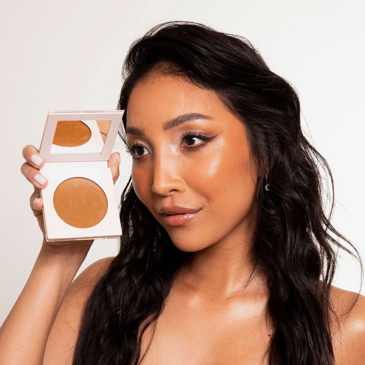 Eine Frau mit strahlendem warmen Make-up lächelt in die Kamera und einen Infinity Bronzer in der Farbe Endless von LH Cosmetics.