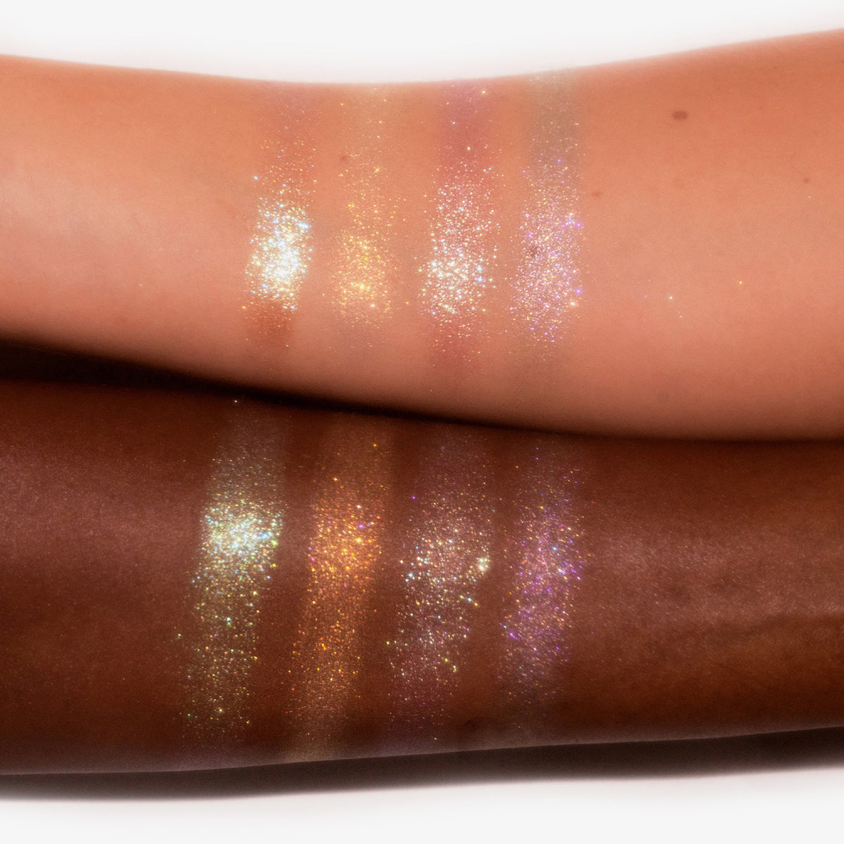 Zwei Arme mit unterschiedlichen Hauttönen zeigen vier schimmernde Farbmuster aus der Shimmer Saga Palette von LH Cosmetics.