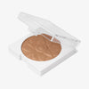 Nahaufnahme des offenen OFRA Pure Glow Finishing Powders in Dark, das feine, schimmernde Puder mit Wellenstruktur zeigt, in transparenter Dose.