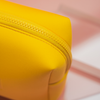 Nahaufnahme einer gelben Kosmetiktasche mit Reißverschluss. Die glatte, leicht matte Oberfläche wirkt weich.
