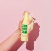 Eine Hand hält die gelbe Rapid Banana Whip-Flasche vor einem rosa Hintergrund.