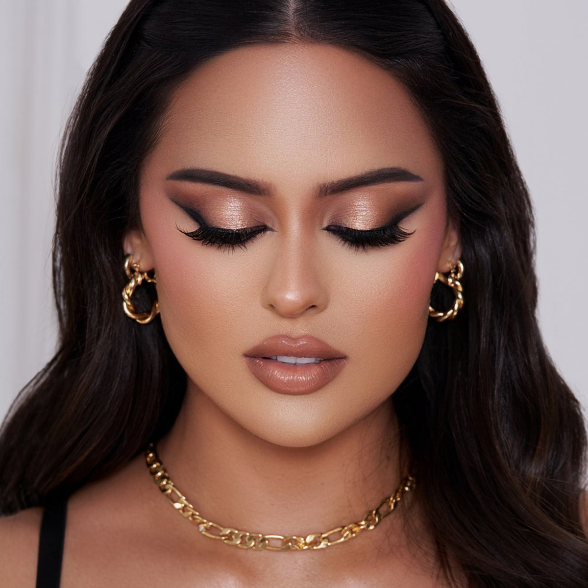 Frau mit langem dunklem Haar, Goldschmuck und glamourösem Make-up mit kräftigem Eyeliner und nudefarbenem Lippenstift, kreiert mit der Essential Palette.