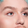 Nahaufnahme einer Person mit blauem Haar und blauen Augen, rotem Lidstrich und langen definierten Wimpern, die mit der Infinity Power Lash Lengthening Mascara von LH Cosmetics betont wurden.