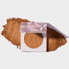 Infinity Bronzer Endless von LH Cosmetics auf losem orange-braunem Puder auf weißem Hintergrund.