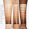 Swatches aller 13 Farbtöne des NABLA Re-Generation Concealers nebeneinander auf drei unterschiedlich hellen Hauttönen aufgetragen – von oben nach unten. Die cremige Textur reflektiert das Licht mit einem leicht glänzenden Finish.