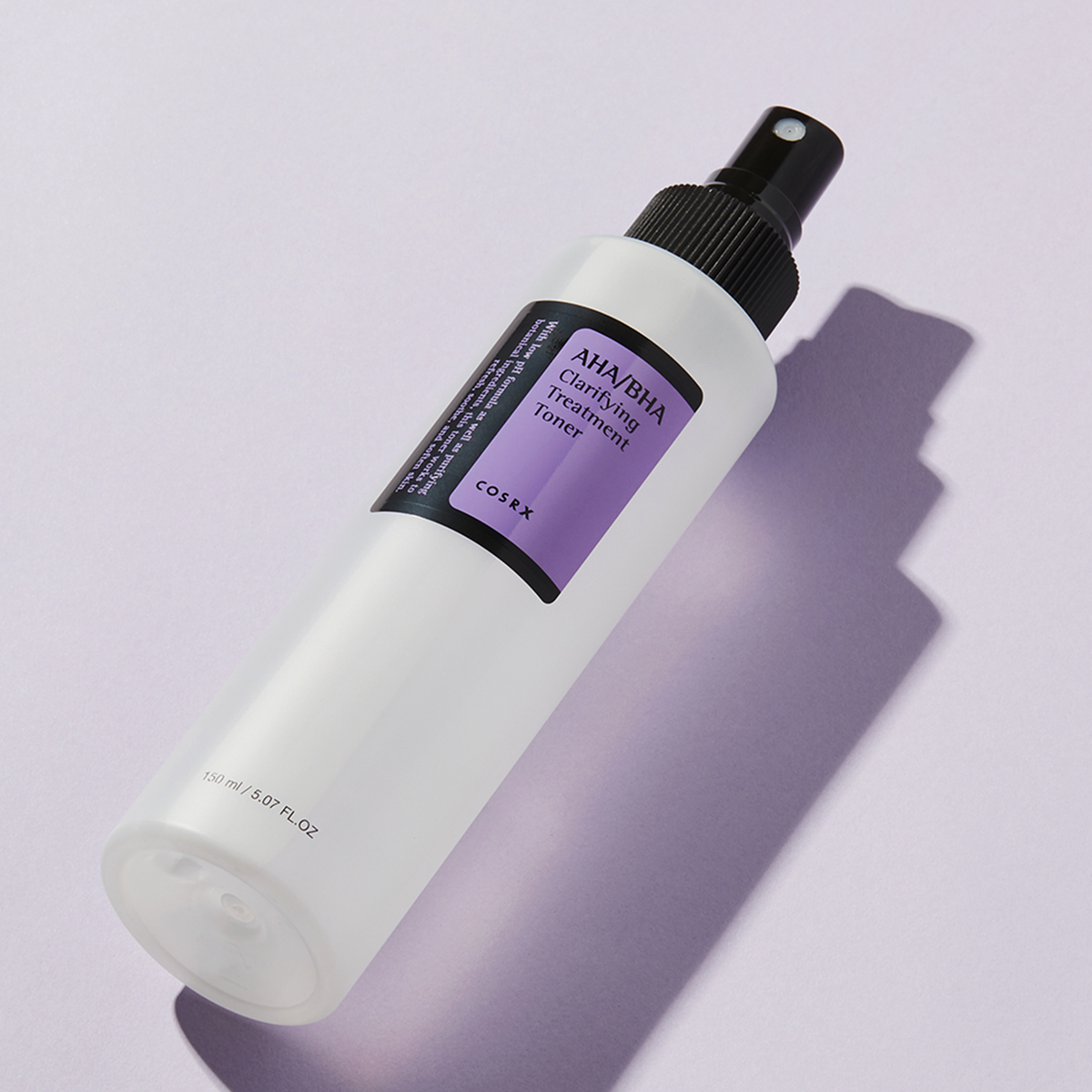AHA/BHA Clarifying Treatment Toner in einer transparenten Sprühflasche ist auf einer hellvioletten Oberfläche abgebildet.