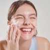 Eine lächelnde Frau wäscht ihr Gesicht mit dem Low-pH Good Morning Gel Cleanser und berührt sanft ihre Wangen.