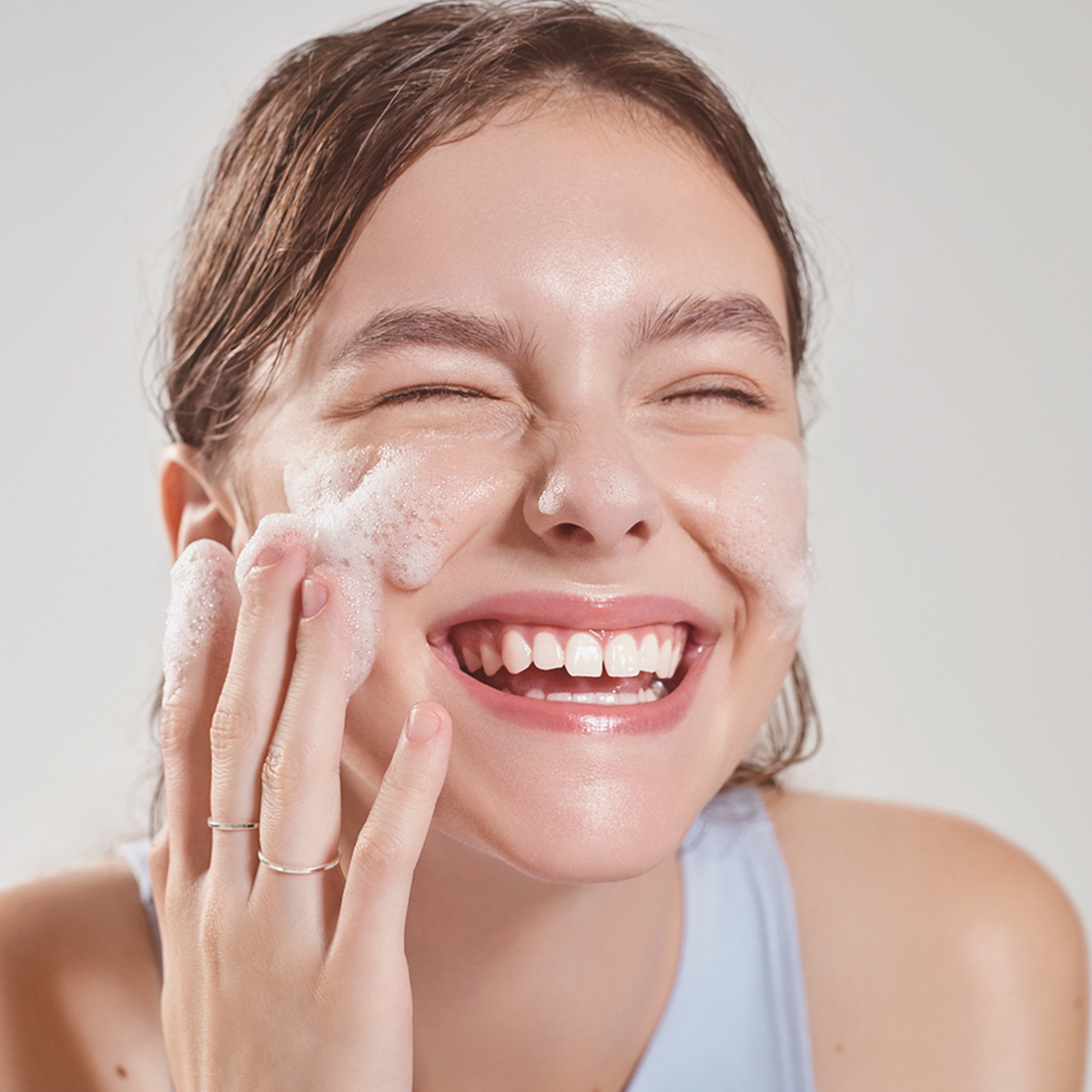 Eine lächelnde Frau wäscht ihr Gesicht mit dem Low-pH Good Morning Gel Cleanser und berührt sanft ihre Wangen.