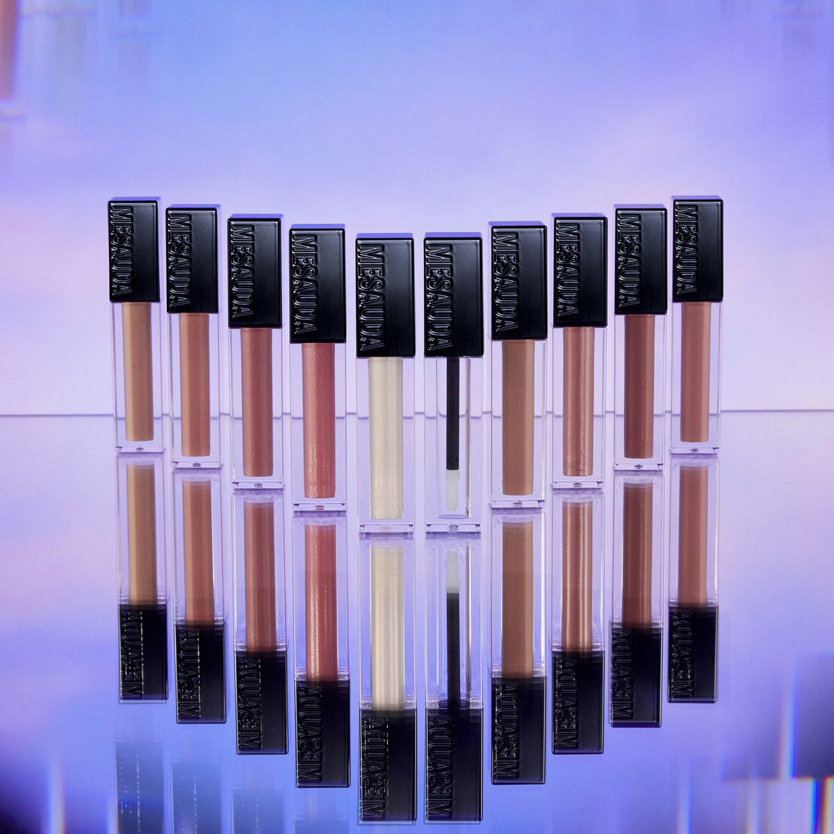 Die 10 Farben des Gloss Matrix Lipglosses von Mesauda Beauty nebeneinander präsentiert und stehen dabei auf einer reflektierenden Fläche.
